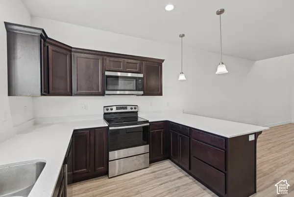 Kitchen featuring dark wood-finish cabinetry, light-toned countertops, stainless steel appliances, and pendant lighting