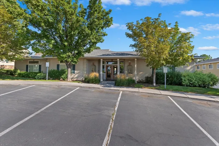Building exterior with a covered entry, mature trees, and an asphalt parking area