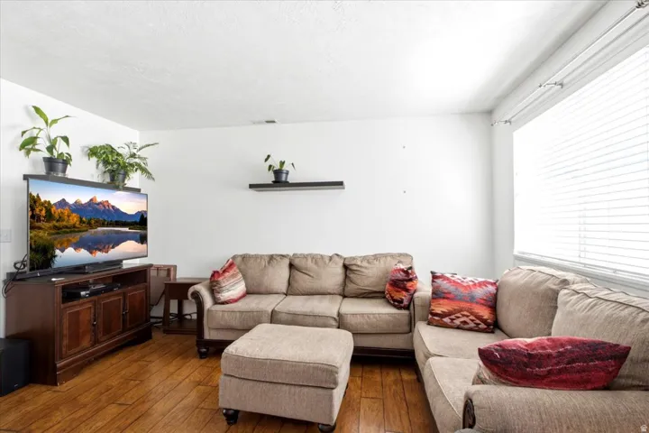 Living area featuring wood-finish flooring, white walls, and a large window with horizontal blinds