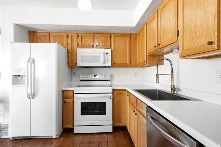 Kitchen featuring wood-finish cabinetry, white countertops, a stainless steel dishwasher, and a double basin sink with a pull-down faucet