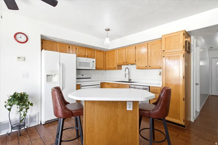 Kitchen featuring wood-finish flooring, white appliances, light wood cabinetry, white countertops, and a peninsula with seating