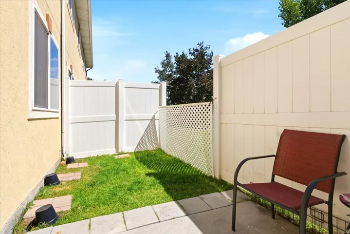 Private outdoor patio space featuring a concrete paver surface, a grass area, and a white privacy fence