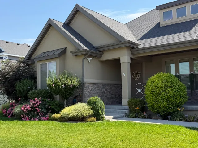 Stucco and stone exterior featuring a covered porch entry, dormer windows, and a manicured lawn with mature landscaping