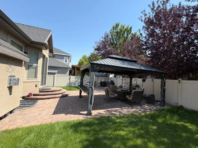 Expansive backyard featuring a manicured lawn, a large paver patio, a permanent metal gazebo, and mature trees