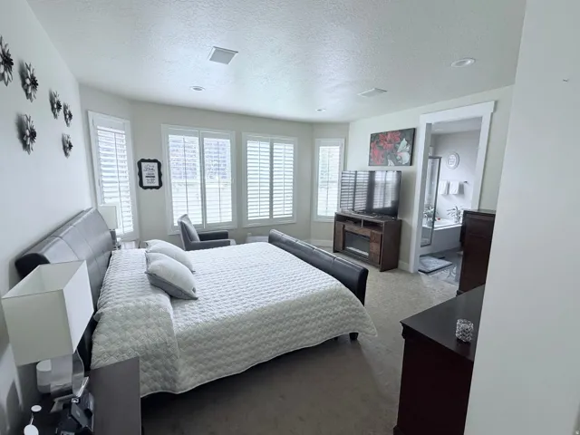 Spacious bedroom featuring multiple windows with plantation shutters, recessed lighting, and an attached bathroom with a built-in tub