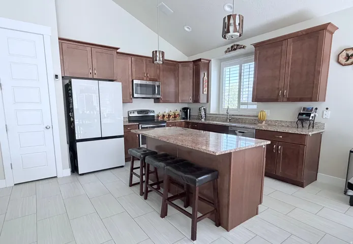 Spacious kitchen featuring a central island with granite countertop, abundant wood cabinetry, stainless steel appliances, and wood-finish tile flooring