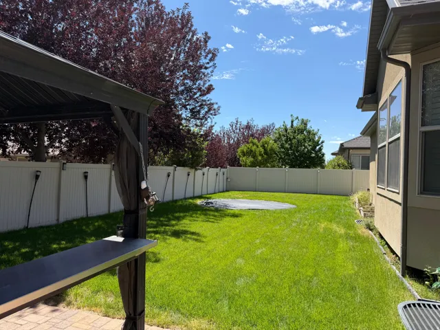 Expansive backyard featuring a green lawn, full privacy fencing, mature landscaping, and a covered patio with a built-in bar