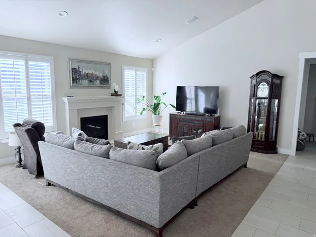 Living area featuring a fireplace with a white mantel, plantation shutters, recessed lighting, vaulted ceilings, and carpet flooring