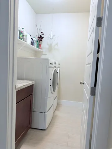 Laundry area featuring light-toned tile flooring, built-in shelving, and a dark wood-finish cabinet with a light speckled countertop