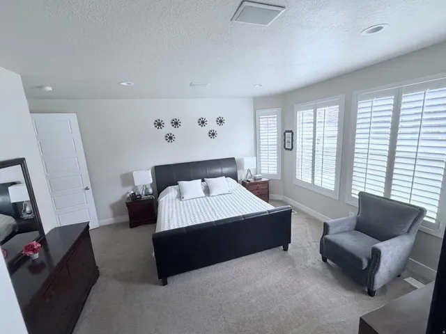 Carpeted bedroom featuring multiple windows with louvered shutters, a paneled door, recessed lighting, and a square ceiling vent