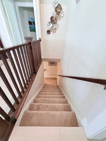 Staircase featuring wood-finish railing, carpeted treads, and a contrasting light-toned tile landing