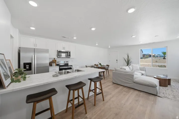 Open-concept living space featuring a kitchen island with seating, stainless steel appliances, white cabinetry, recessed lighting, and wood-finish flooring