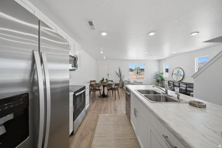 Open-concept living space featuring a kitchen island with dual stainless steel sink, wood-finish flooring, and recessed lighting