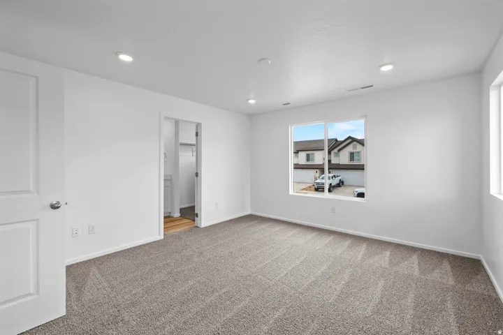 Spacious room with plush gray carpeting, recessed ceiling lighting, and a large window providing natural illumination