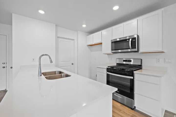 Modern kitchen featuring white cabinetry, light-toned countertops, a stainless steel gas range, a coordinating microwave, and a double basin sink with a chrome faucet
