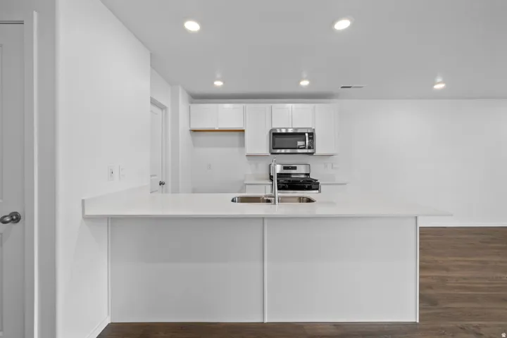 Kitchen featuring a white countertop island with an undermount sink, stainless steel appliances, white cabinetry, and recessed lighting