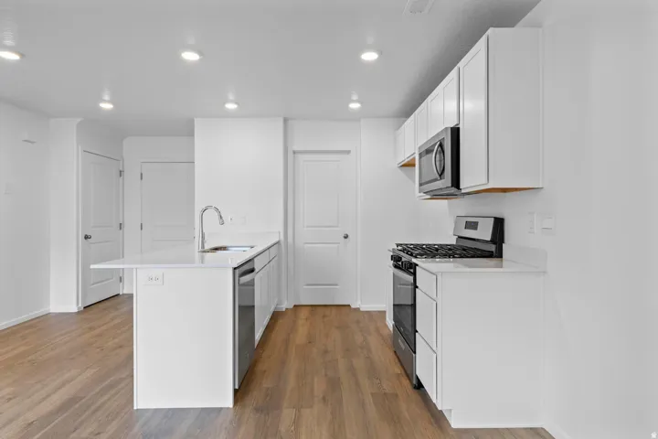 Kitchen featuring white cabinetry, light-toned countertops, a stainless steel gas range, a coordinating microwave, and wood-finish flooring