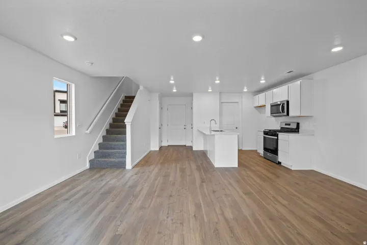 Open-concept living space featuring wood-finish flooring, recessed lighting, and a white kitchen with stainless steel appliances
