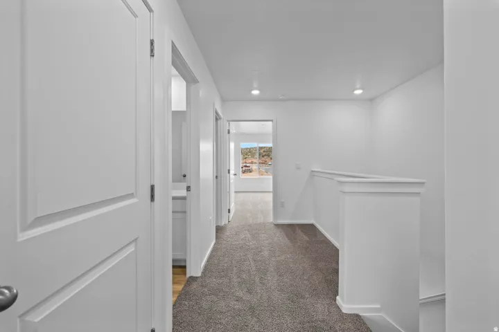 Carpeted hallway with white walls and trim, featuring recessed lighting, panel doors, and a partial balustrade