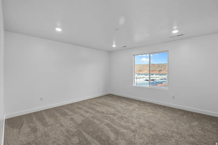 Spacious room featuring neutral carpeting, white walls, recessed ceiling lighting, and a large window providing natural illumination and a distant mountain backdrop