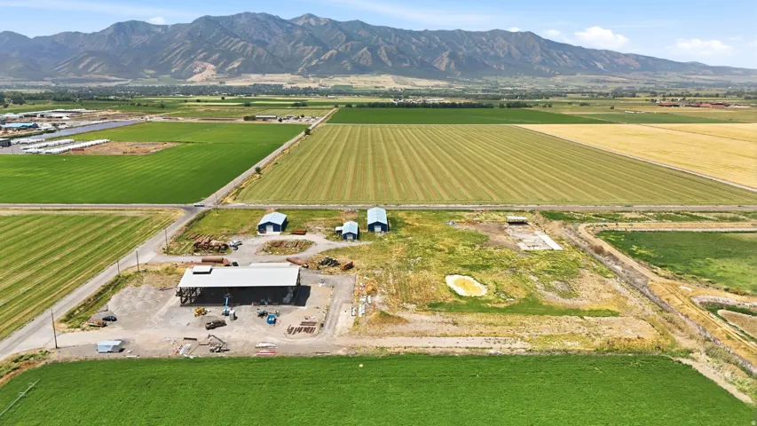 Expansive agricultural property featuring multiple outbuildings, cultivated fields, and a mountainous backdrop