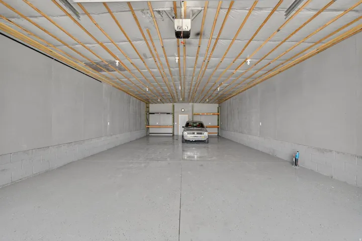 Spacious garage featuring an epoxy-coated concrete floor, concrete block base walls, and a finished ceiling with exposed wood framing