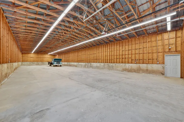 Spacious warehouse interior featuring a concrete floor, exposed wood beam ceiling, and ample overhead strip lighting