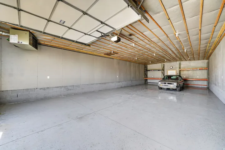 Spacious garage featuring an epoxy-coated concrete floor, exposed wood beam ceiling, attached garage door opener, and wall-mounted heating unit