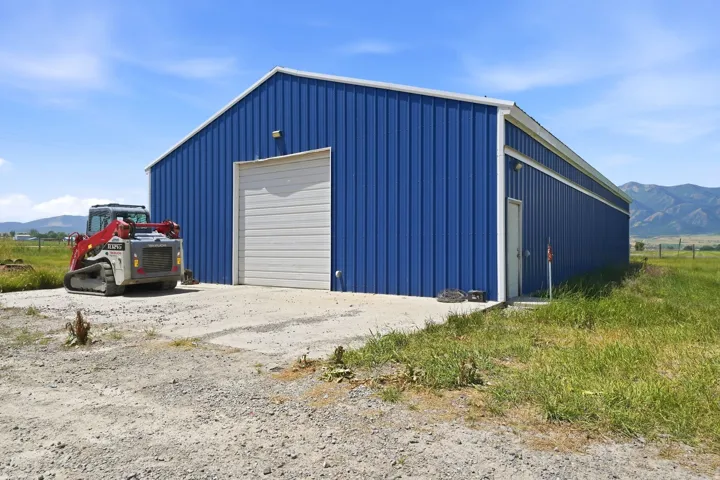 Blue metal-sided barn featuring a large roll-up door, a separate pedestrian entry door, concrete apron, and a gravel drive