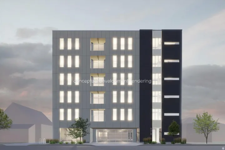 Contemporary building exterior featuring a light gray facade with vertical window accents, a contrasting dark gray section with horizontal windows, and ground-level plantings