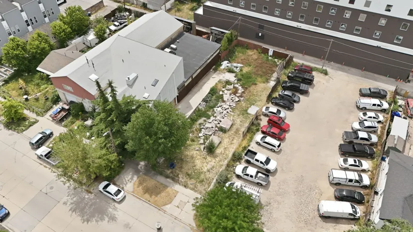 Expansive gravel parking lot with marked spaces for multiple vehicles, bordered by a concrete street and an adjacent building