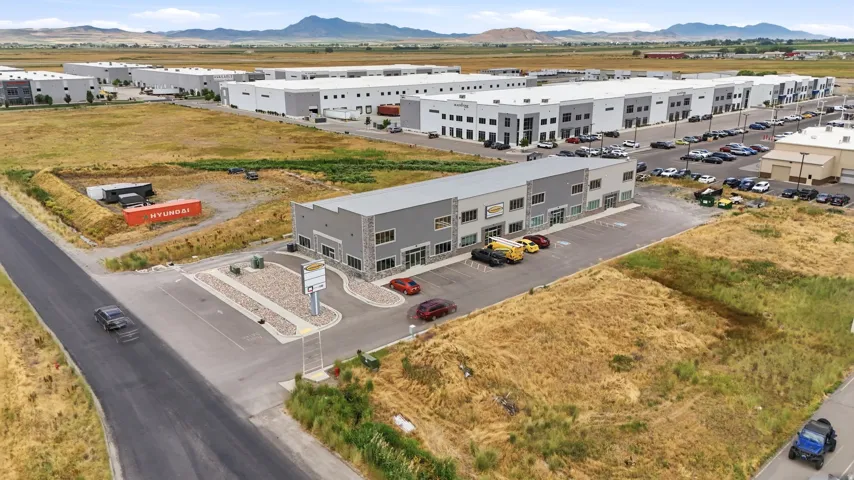 Modern commercial building featuring a gray facade with stone accents, a paved parking area, and mature landscaping