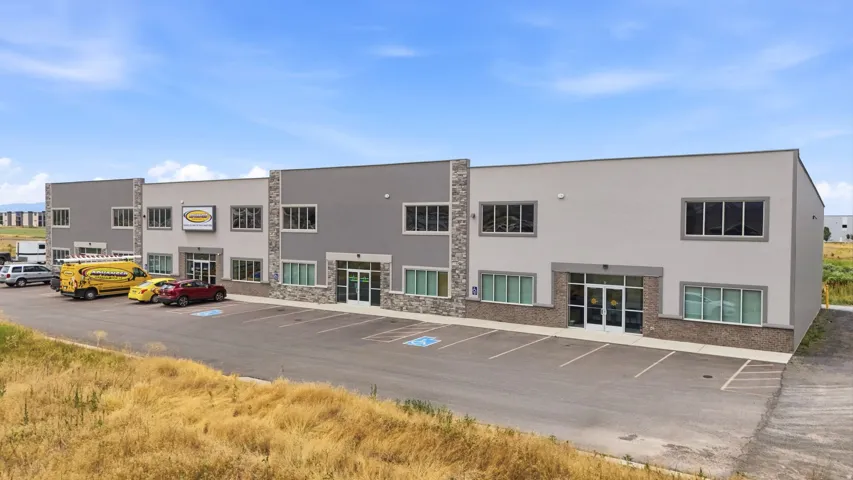 Contemporary commercial building featuring a multi-tone facade with stone accents, multiple large windows, and a dedicated asphalt parking area