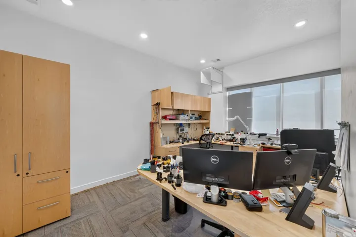 Office space featuring a wall of windows with roller shades, recessed lighting, wood-finish built-in cabinetry, and patterned carpet flooring