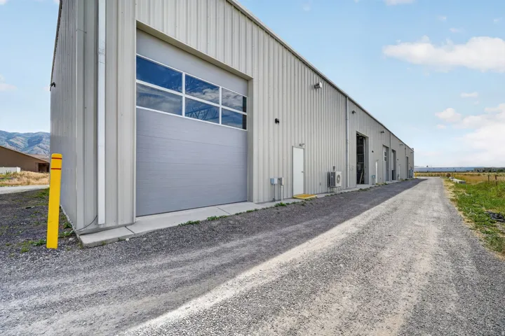 Industrial building featuring corrugated metal siding, multiple roll-up doors with upper windows, and a gravel driveway