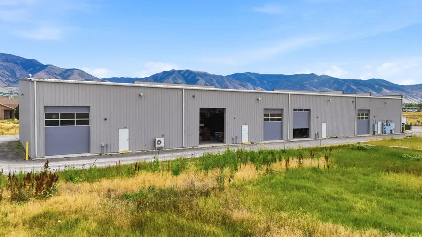 Industrial-style building featuring corrugated metal siding, multiple roll-up garage doors, and individual entry doors