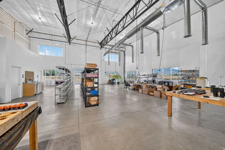 Spacious warehouse interior featuring high ceilings, concrete flooring, exposed ductwork, large windows, and multiple work areas