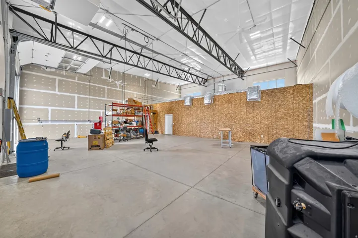 Expansive industrial interior featuring a large roll-up door, exposed metal beam ceiling with white panels, and concrete flooring