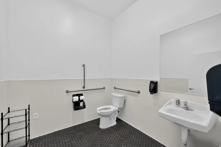 Restroom featuring a white wall-mounted sink, a wall-mounted mirror, a standard toilet, and hexagonal black tile flooring