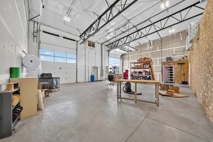 Spacious industrial interior featuring concrete flooring, exposed ceiling trusses, and two large overhead doors with upper window panels