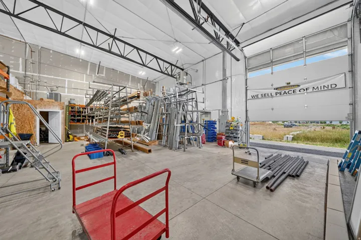 High-ceiling industrial interior featuring a large roll-up door, exposed metal beam ceiling structure, and concrete flooring