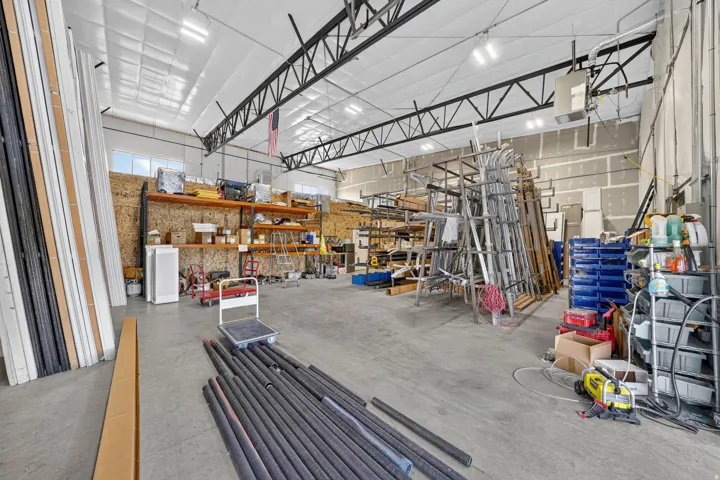 Spacious industrial interior featuring a high ceiling with exposed trusses, concrete flooring, and multiple overhead light fixtures