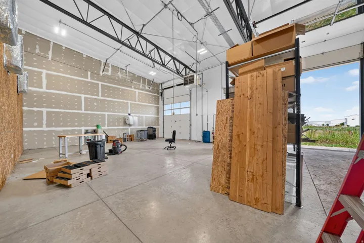 Spacious warehouse interior featuring a high ceiling with exposed trusses, concrete flooring, and multiple overhead doors for access