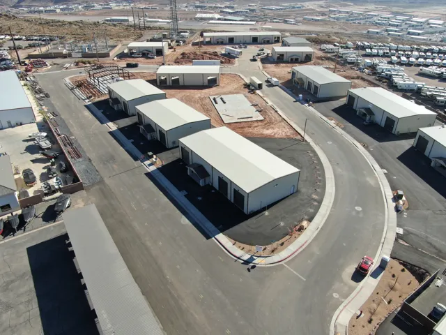 Industrial park featuring multiple buildings with metal siding and roofs, paved roadways, and landscaped perimeters