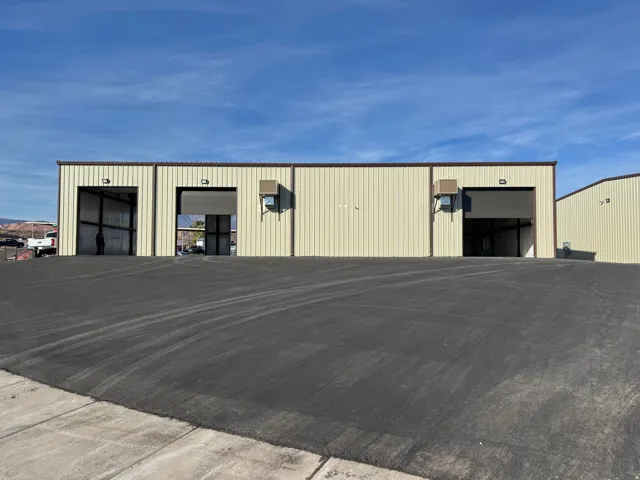 Commercial building featuring multiple roll-up doors, light-colored metal siding, and a contrasting brown trim