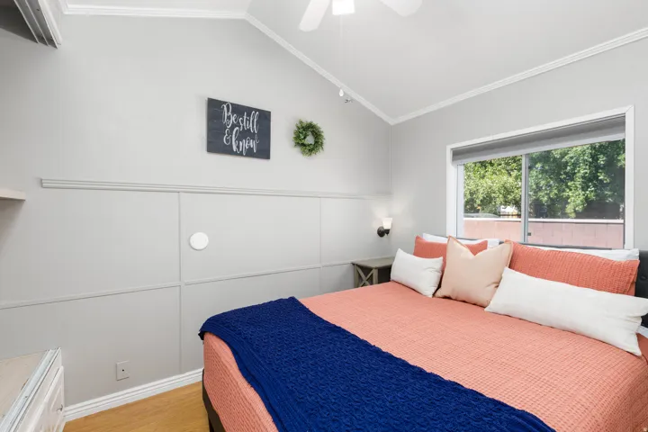 Vaulted ceiling with a ceiling fan, window with roller shade, sconce lighting, and wood-finish flooring