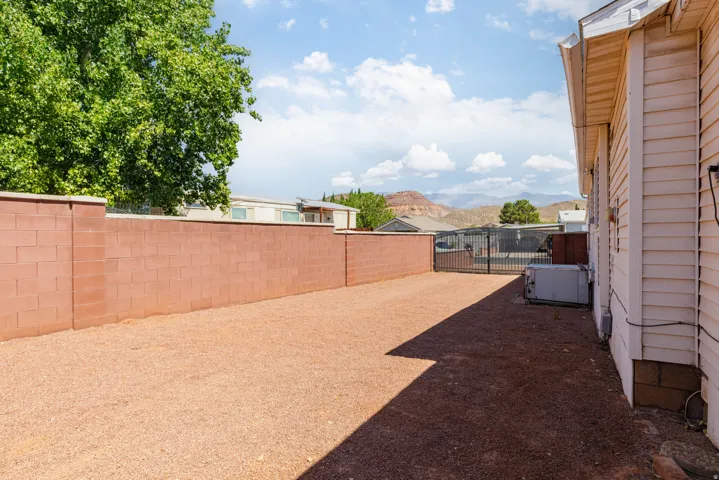 Expansive side yard featuring a crushed rock surface, a full-height block wall, and a dual-door metal gate