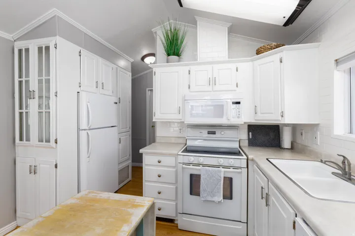 Kitchen featuring white cabinetry, white appliances, light-toned countertops, subway tile backsplash, and wood-finish flooring