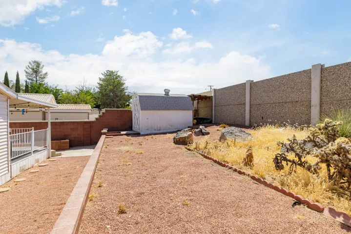 Backyard featuring a detached storage shed, red gravel ground cover, and a textured privacy wall