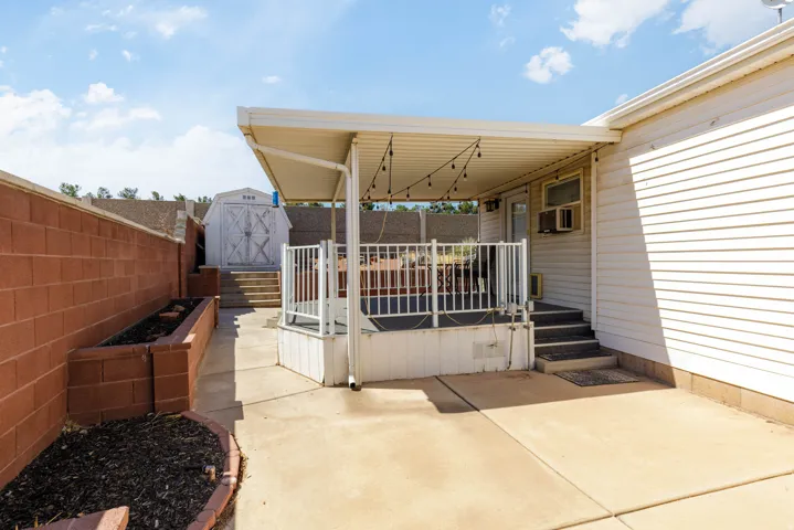 Backyard patio featuring a covered deck with white railing, built-in steps, and concrete flooring